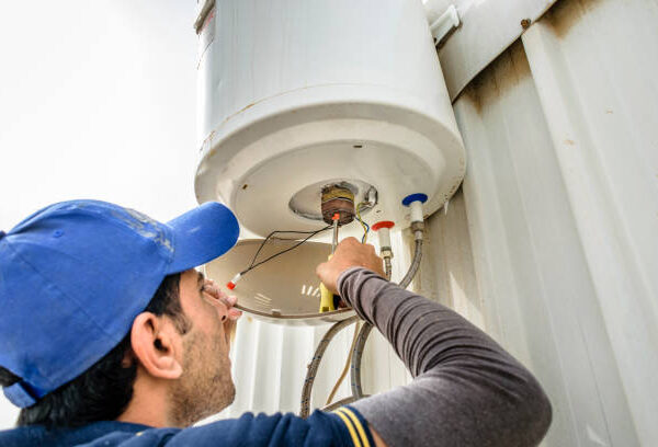 a professional electrician man is fixing a water heater at the roof top and wearing blue uniform and cap